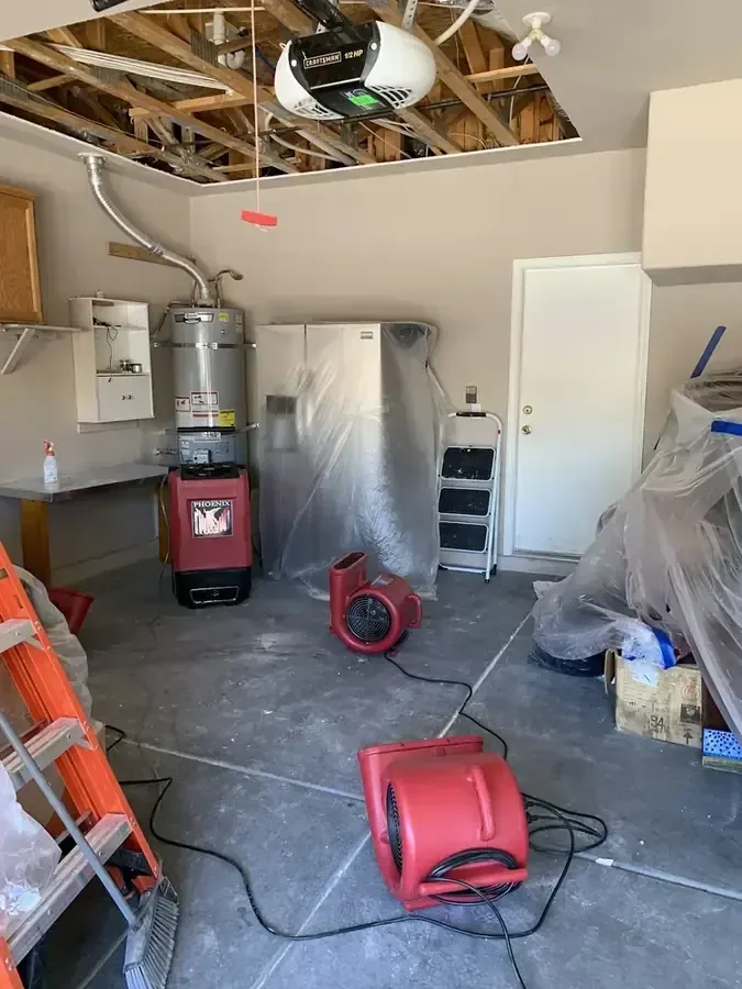 Air movers and a dehumidifier drying a garage with its ceiling opened after a water heater leak