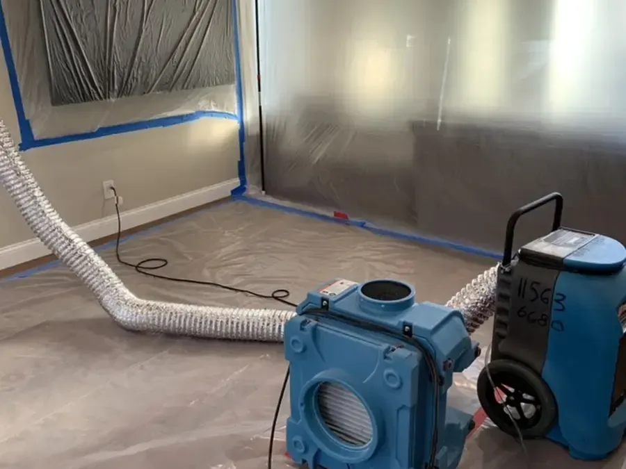 Plastic containment sheeting and a dehumidifier set up inside a room during a water damage dry-out