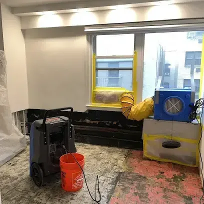 Blue air movers and a dehumidifier running in an emptied room with the floor covering pulled up