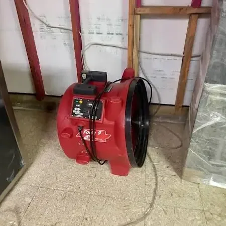 Blue air movers set at the foot of a staircase where the lower walls were cut out to dry