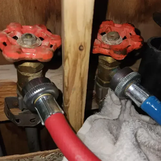 Washer supply hoses on red shutoff valves with a towel soaking up a laundry leak