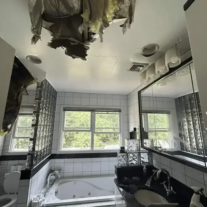 A bathroom ceiling torn open and collapsed after water from a broken pipe above soaked through