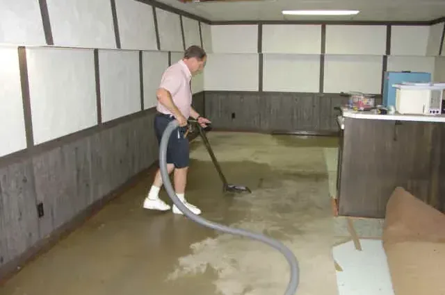 Technician pulling standing water off a finished basement floor with an extraction wand and hose