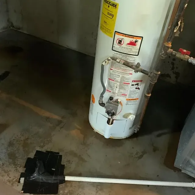 A puddle spreading around the base of a failed tank water heater in a garage